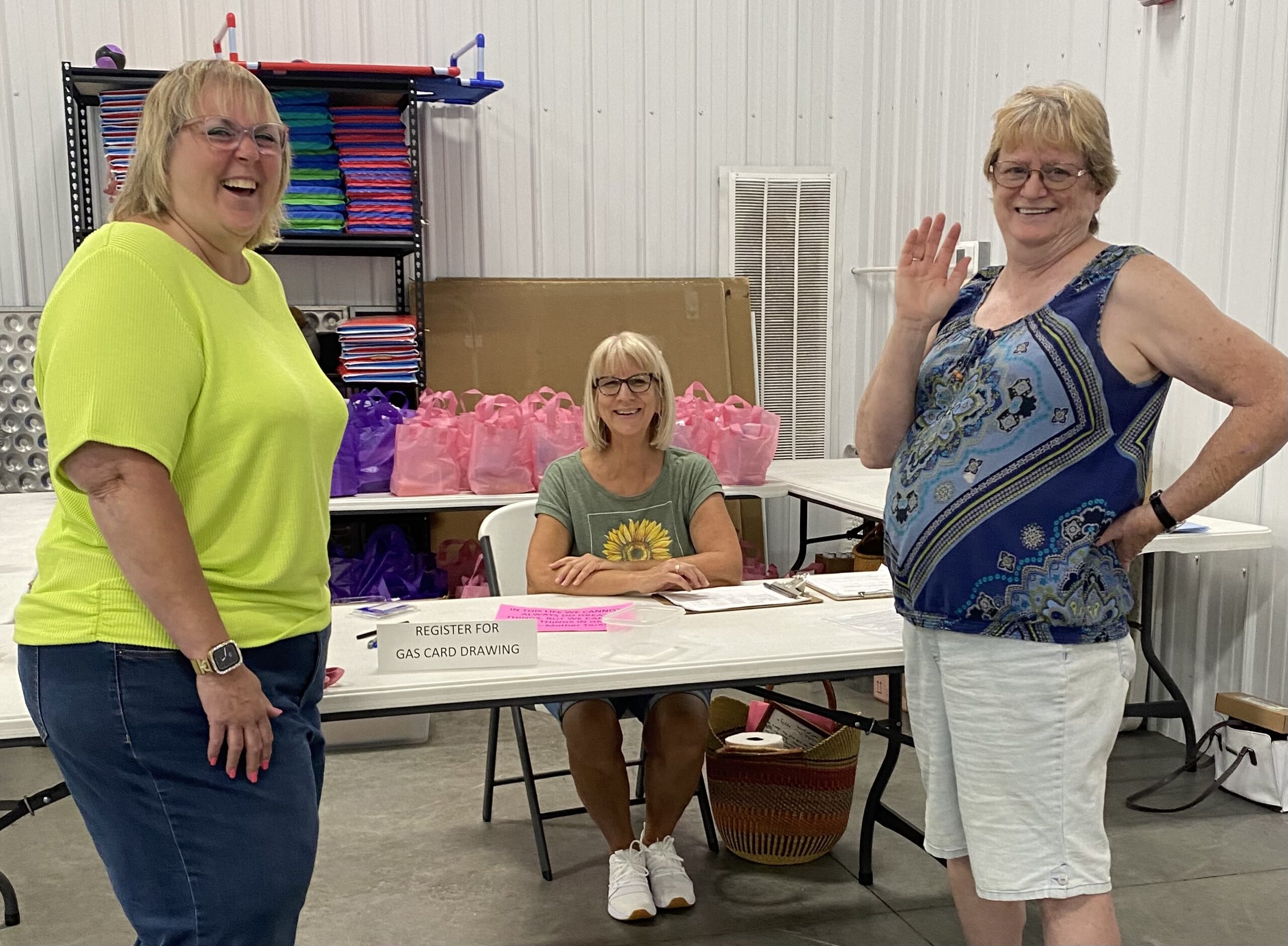 Three women smile at a table displaying a sign that reads "Registration for gas card drawing."