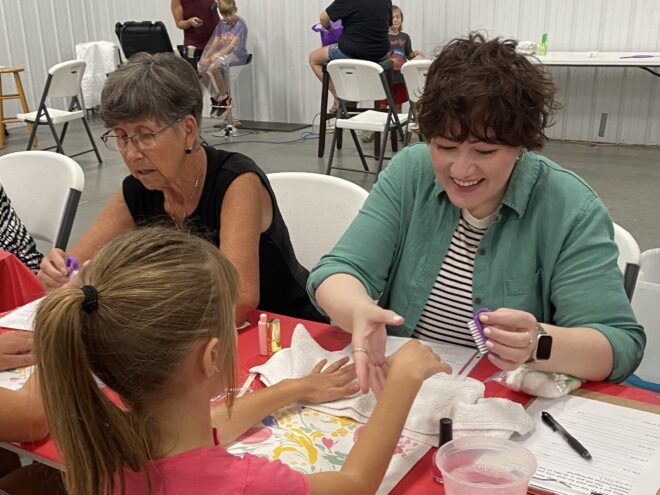 A woman smiles as she paints a young girl's fingernails.