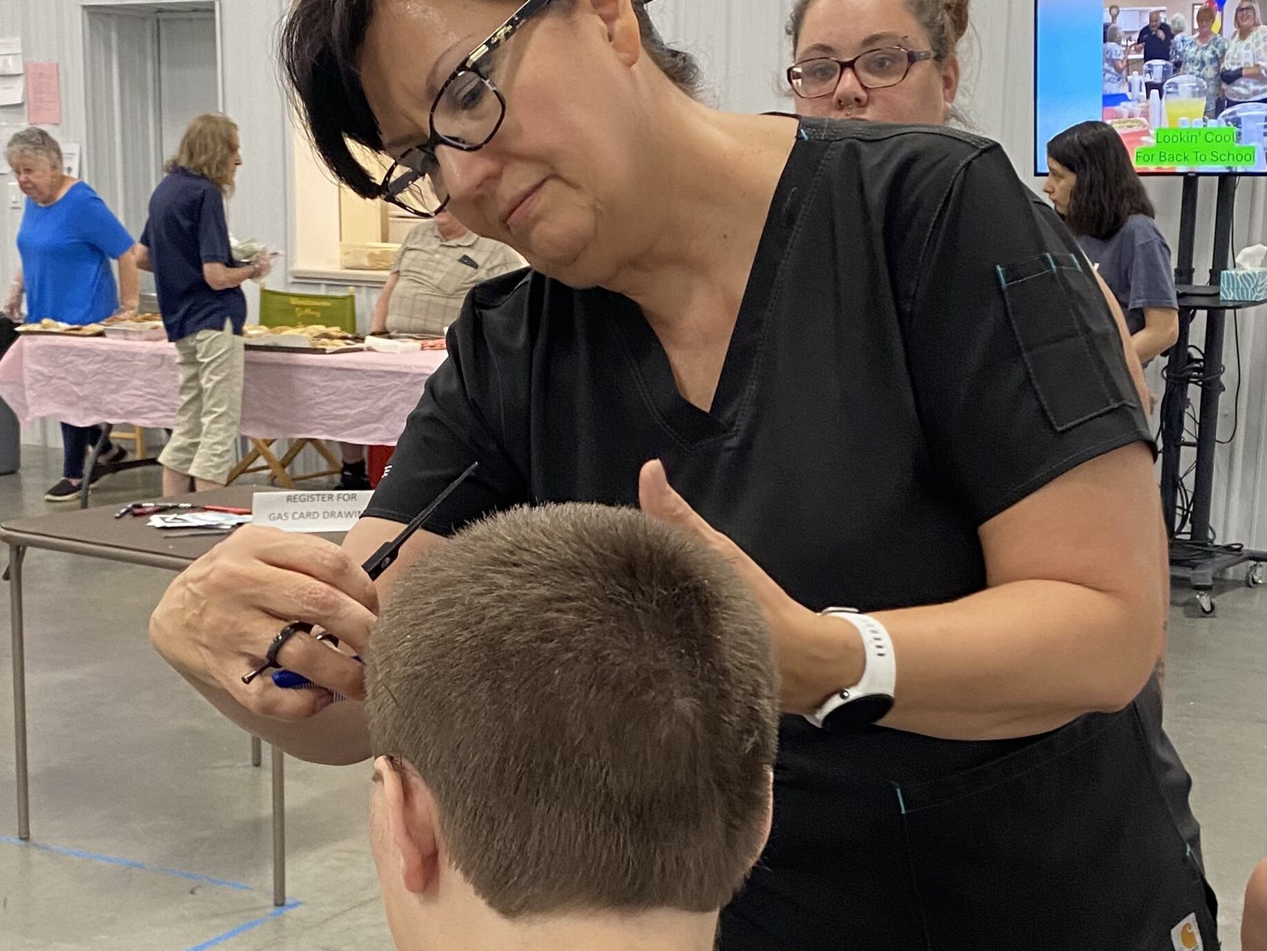 A woman holding scissors prepares to cut a young boys hair.