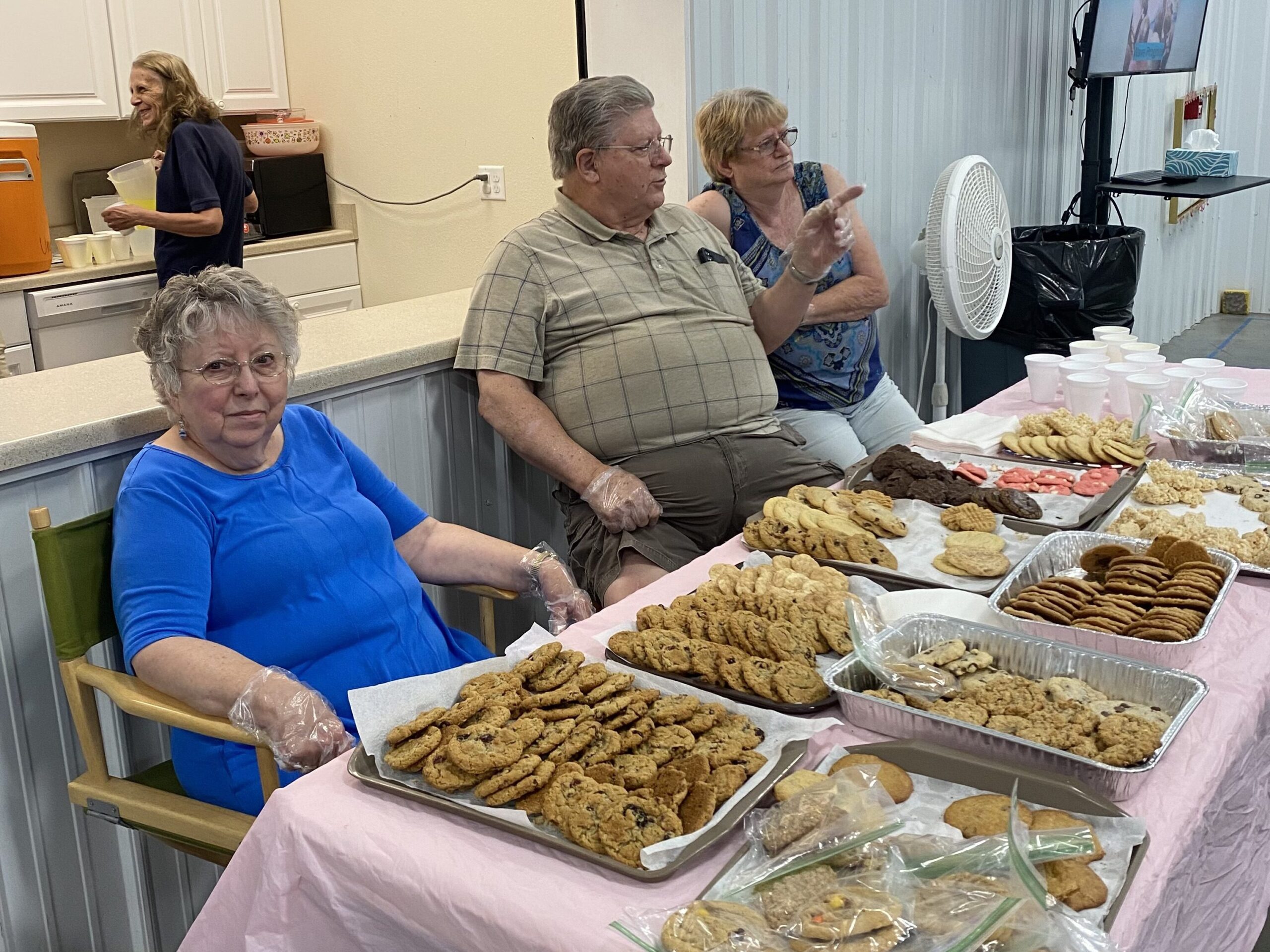 Three volunteers chat while sitting at a table full of cookies.