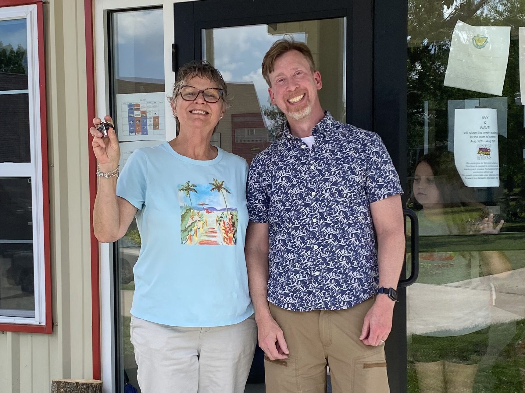 Two volunteers smile as they stand outside the doors of a church.