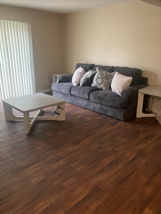 Photo shows a grey couch with 4 throw pillows. In front of the couch is a small coffee table.