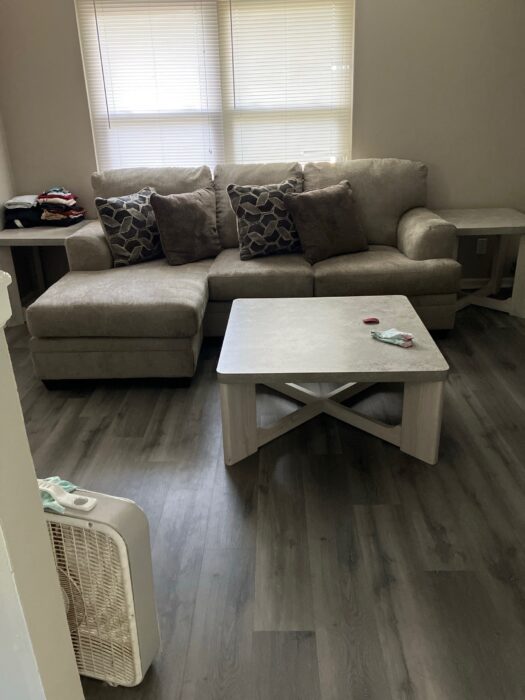 Photo shows a tan L-shaped couch with four throw pillows, and a small coffee table.