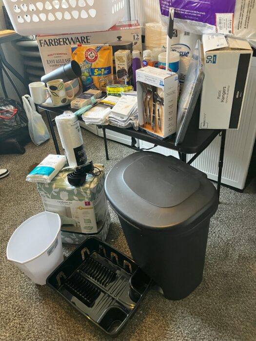 Photo shows various household items, such as a trash can, laundry basket, and cleaning supplies.